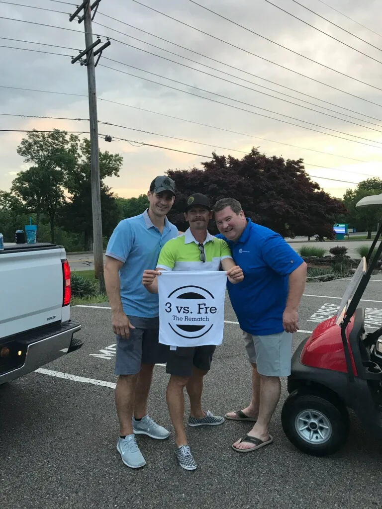 Friends posing with a printed towel beside golf carts